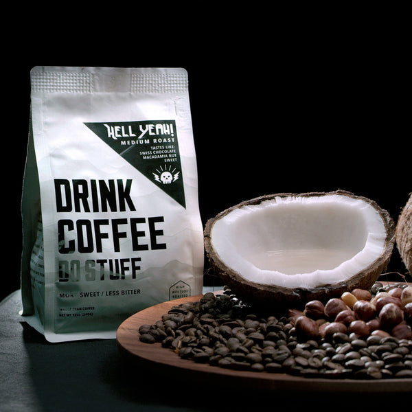Coffee beans, coconuts, and a mug on a dark surface with a coffee bag in the background.