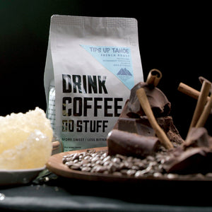 Coffee bag with a plate of coffee beans, chocolate, cinnamon sticks, and honeycomb seen in the foreground.