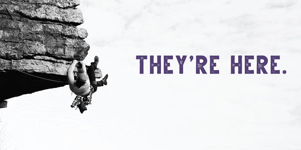 Black and white image of a climber on a rock face with 'THEY'RE HERE.' text in purple.
