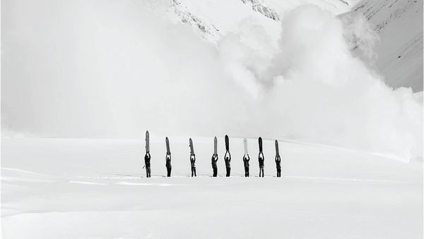 Multiple skis and ski poles arranged in a line on a snowy surface