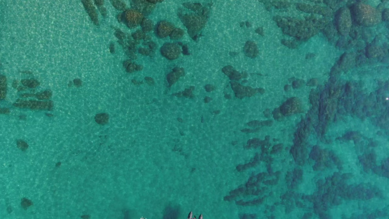 Video is from a drone perspective above Lake Tahoe, showing brilliant turquoise waters with a few boats and boulders.
