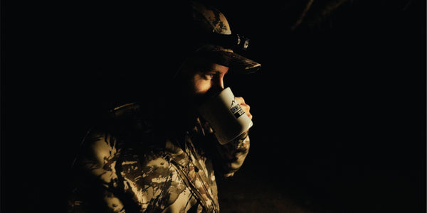 Person in camouflage holding a mug in a dark setting